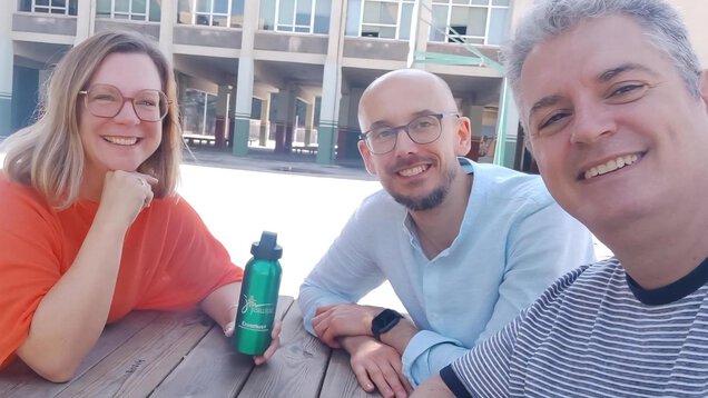 Eine Frau und zwei Männer schauen lächelnd in die Kamera.